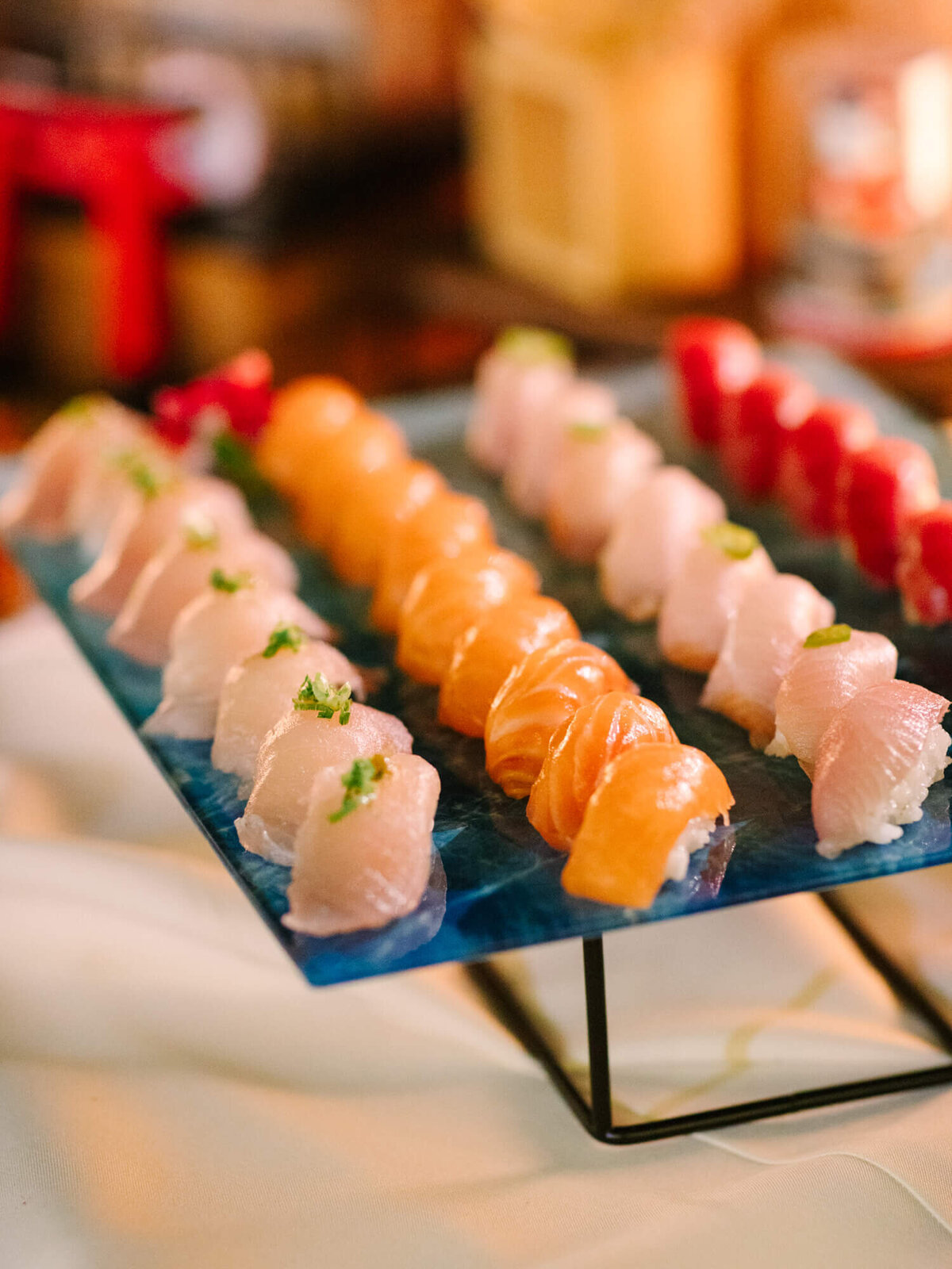 A blue rectangular platter with neatly arranged rows of sushi, featuring salmon and white fish slices on rice.