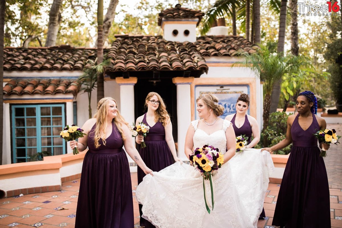 Bridesmaids carry the Bride's train as they walk through the courtyard
