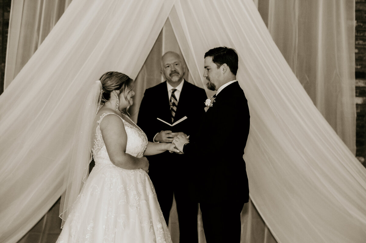 bride and groom standing at the alter of their indoor little rock wedding ceremony as they hold hands and say their vows to each other