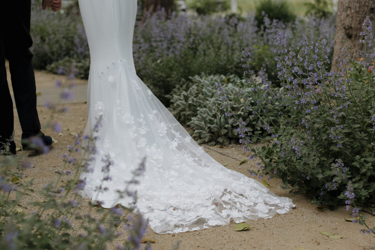 A close-up of a bride’s intricate lace train flowing gracefully along a garden path, surrounded by fragrant lavender blooms.