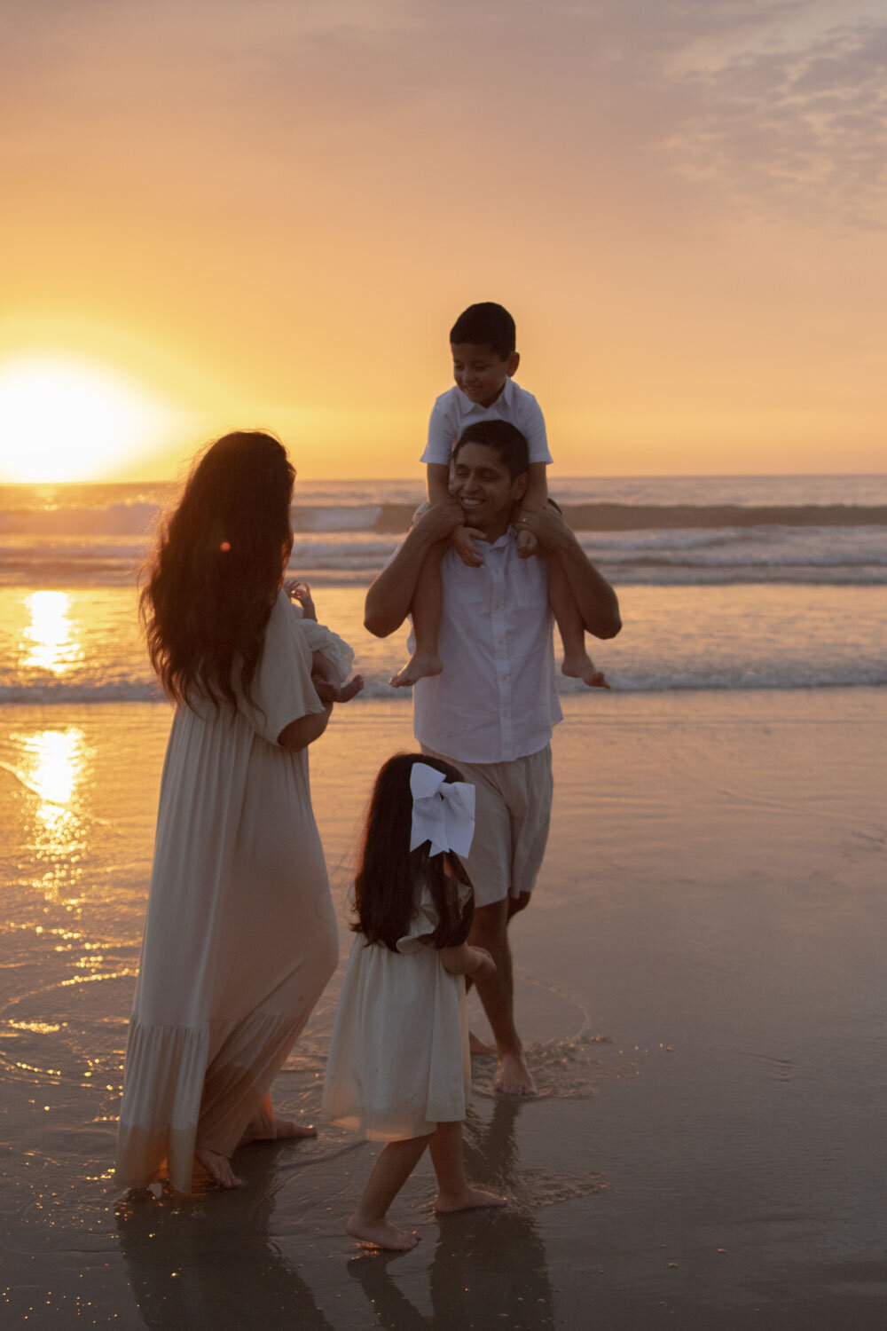 Father carrying his son on his shoulders as they walk along the beach at sunset