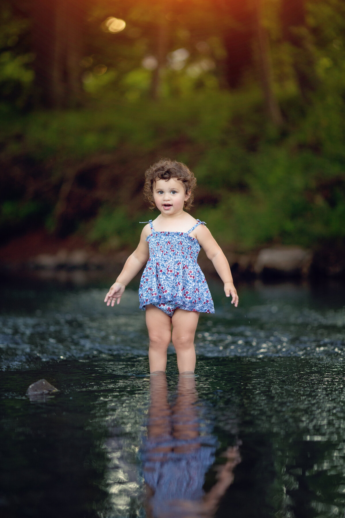 A young girl in a blue floral print bathing suit wades through a shallow river