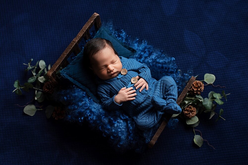 Newborn boy in blue romper posed on little bed