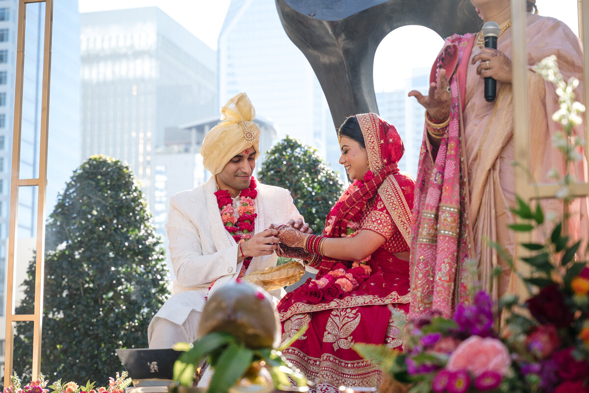 Beautiful Indian wedding ceremony at the Grand Bohemian Hotel Charlotte. The groom in a white sherwani and golden turban places a bracelet on the smiling bride in a red bridal lehenga. Captured by a Charlotte Indian wedding photographer specializing in vibrant and emotional wedding photography.