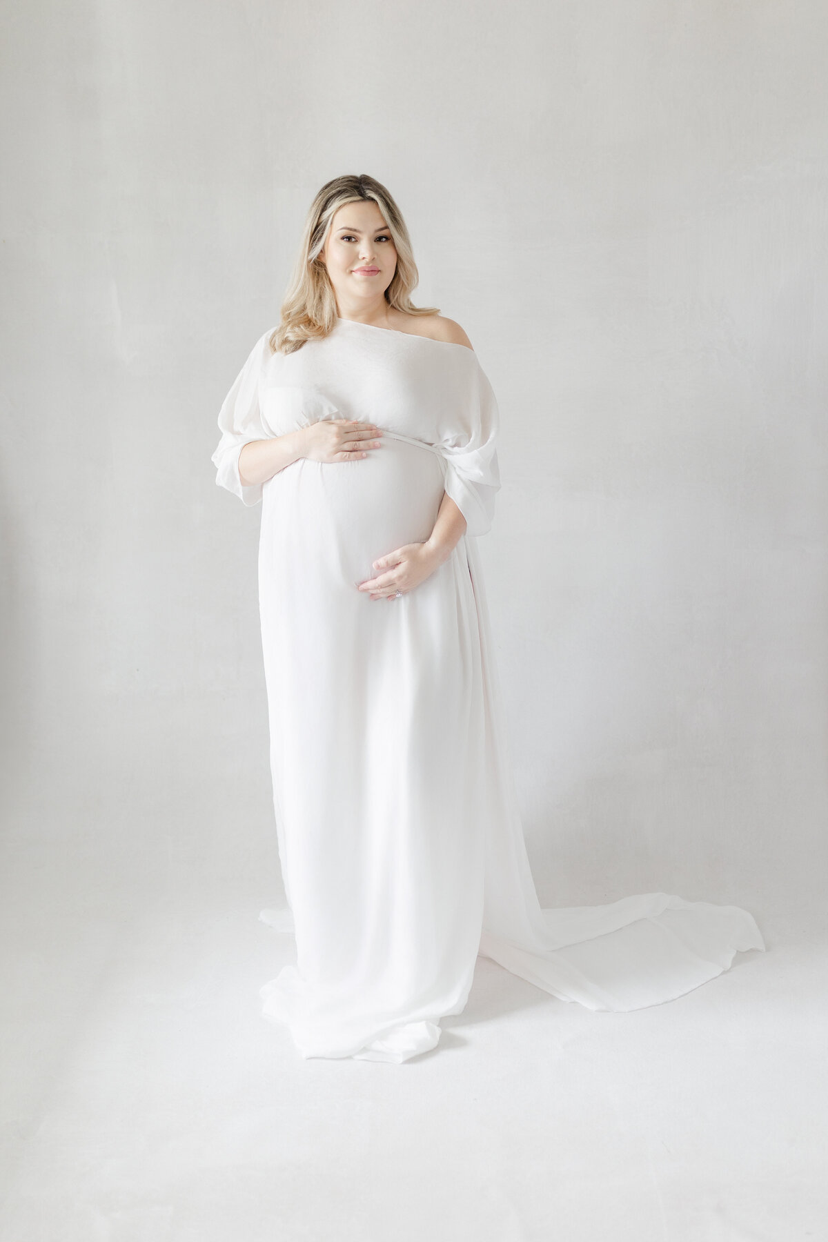 Elegant maternity image of Calli holding baby bump in minimalist white studio