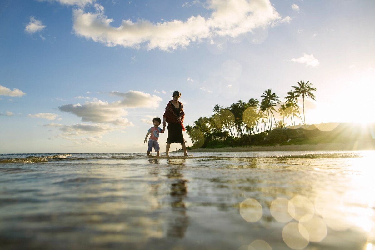 mom and son walk along the shallows of kahala beach at sunset