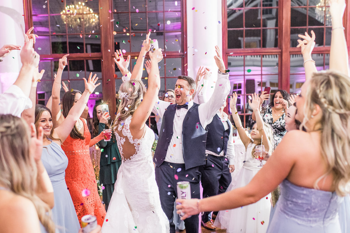 Bride and Groom on their wedding day throwing confetti in the air at the reception with their guests.