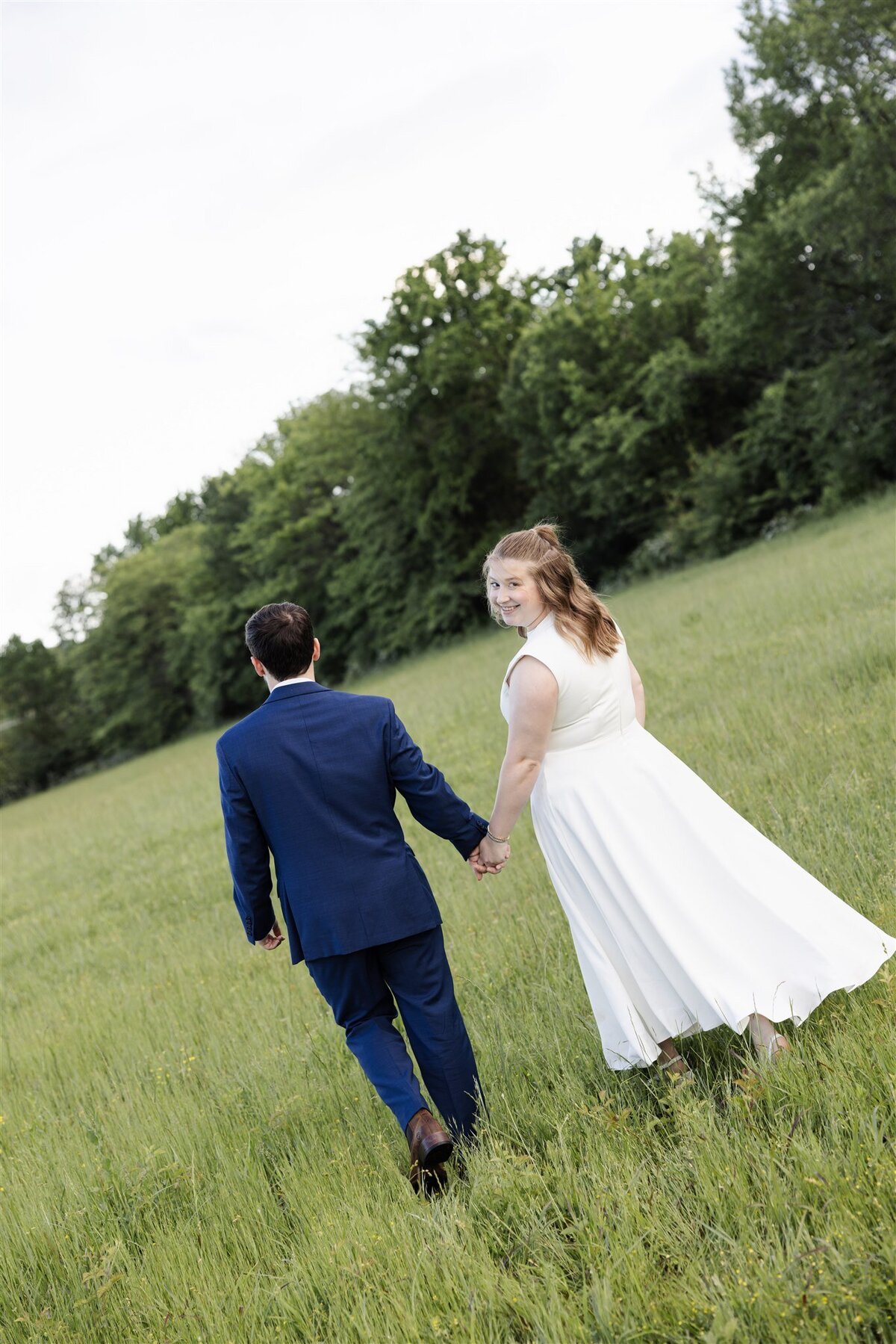 bride and groom holding hands walking through field