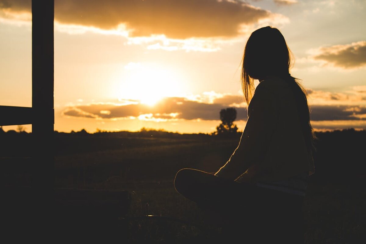 A woman sitting outside looking out at the sunset.