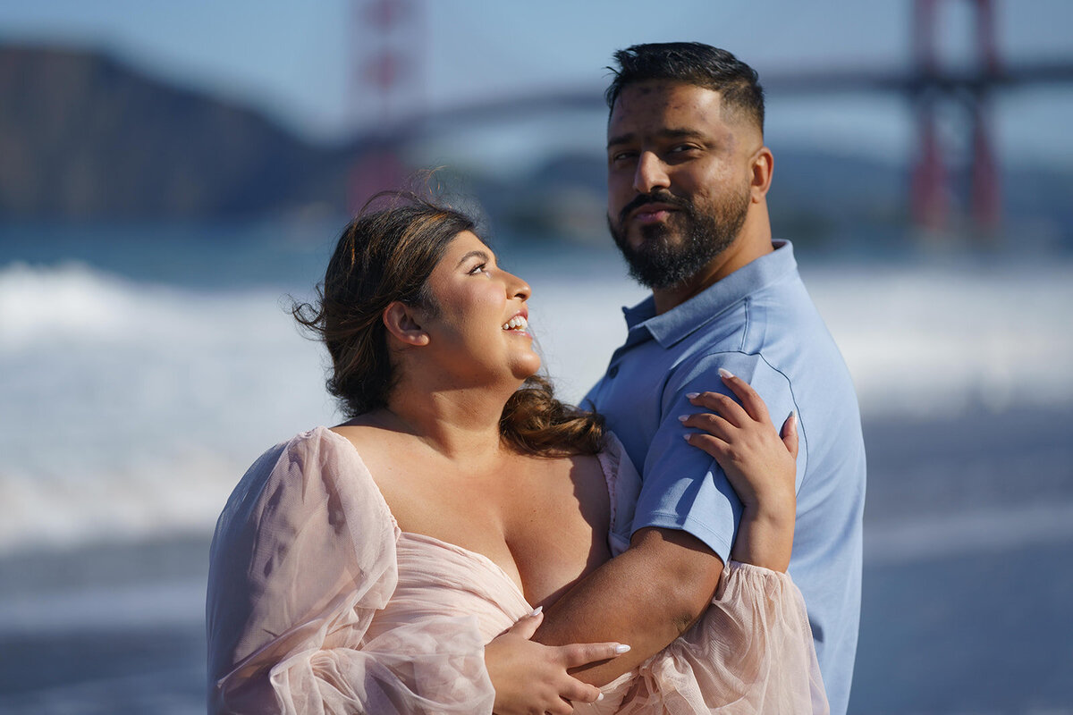 Couple embracing and smiling after a surprise proposal with the golden gate bridge in the background.