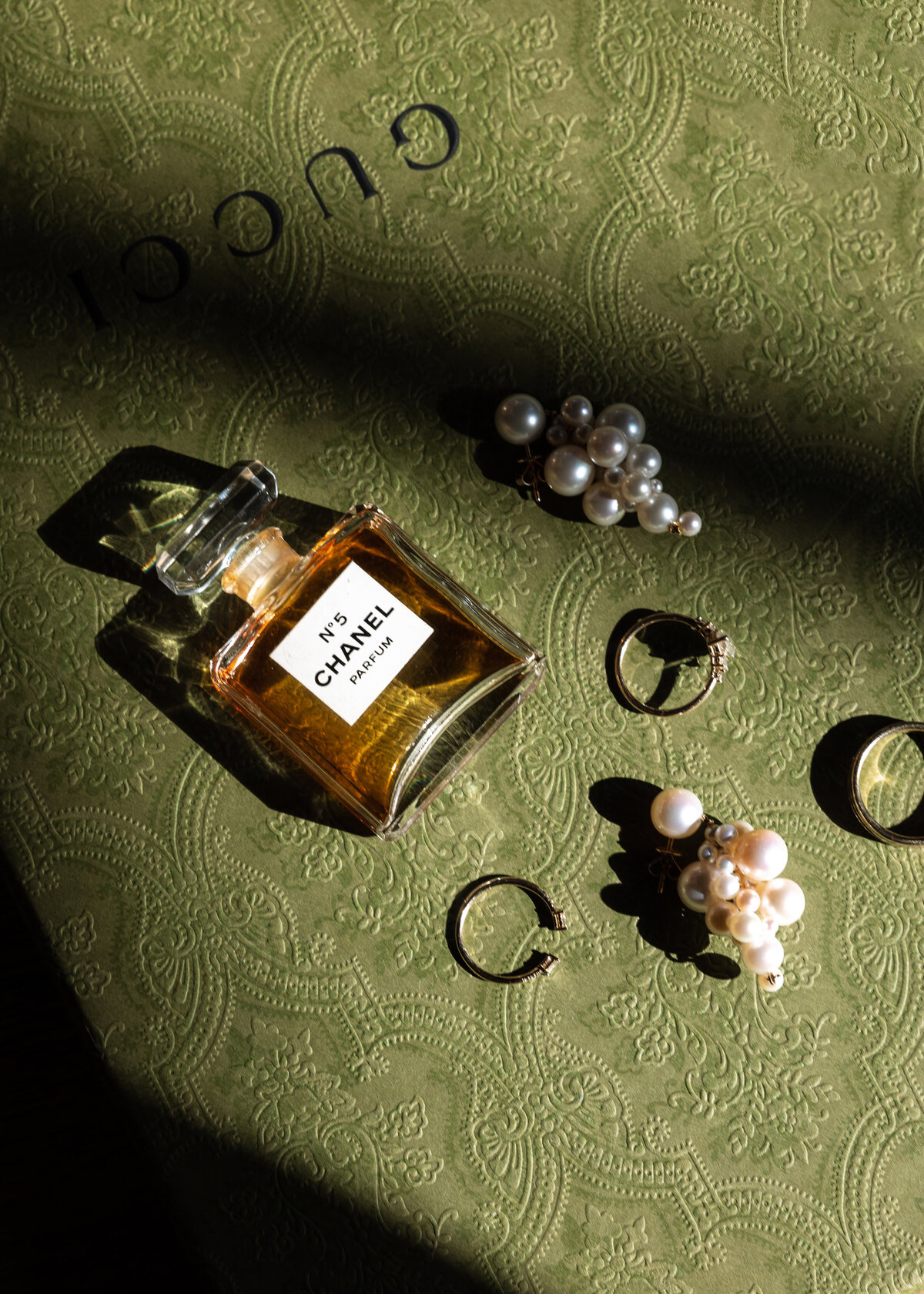 a bottle of perfume, rings and earrings on a green surface