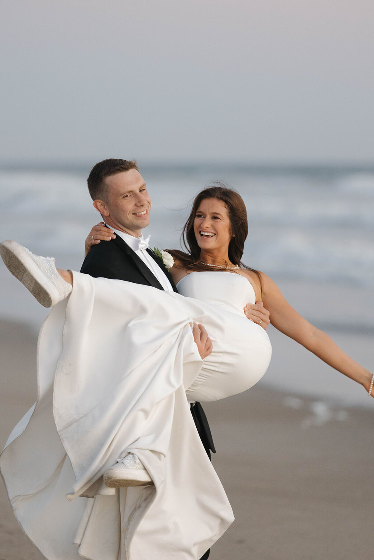 Groom carrying his laughing bride on the beach