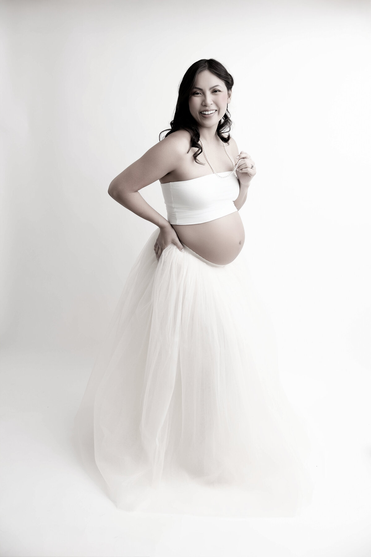 An black and white photo of an expecting mom wearing a white tube top and skirt with pregnant belly showing.