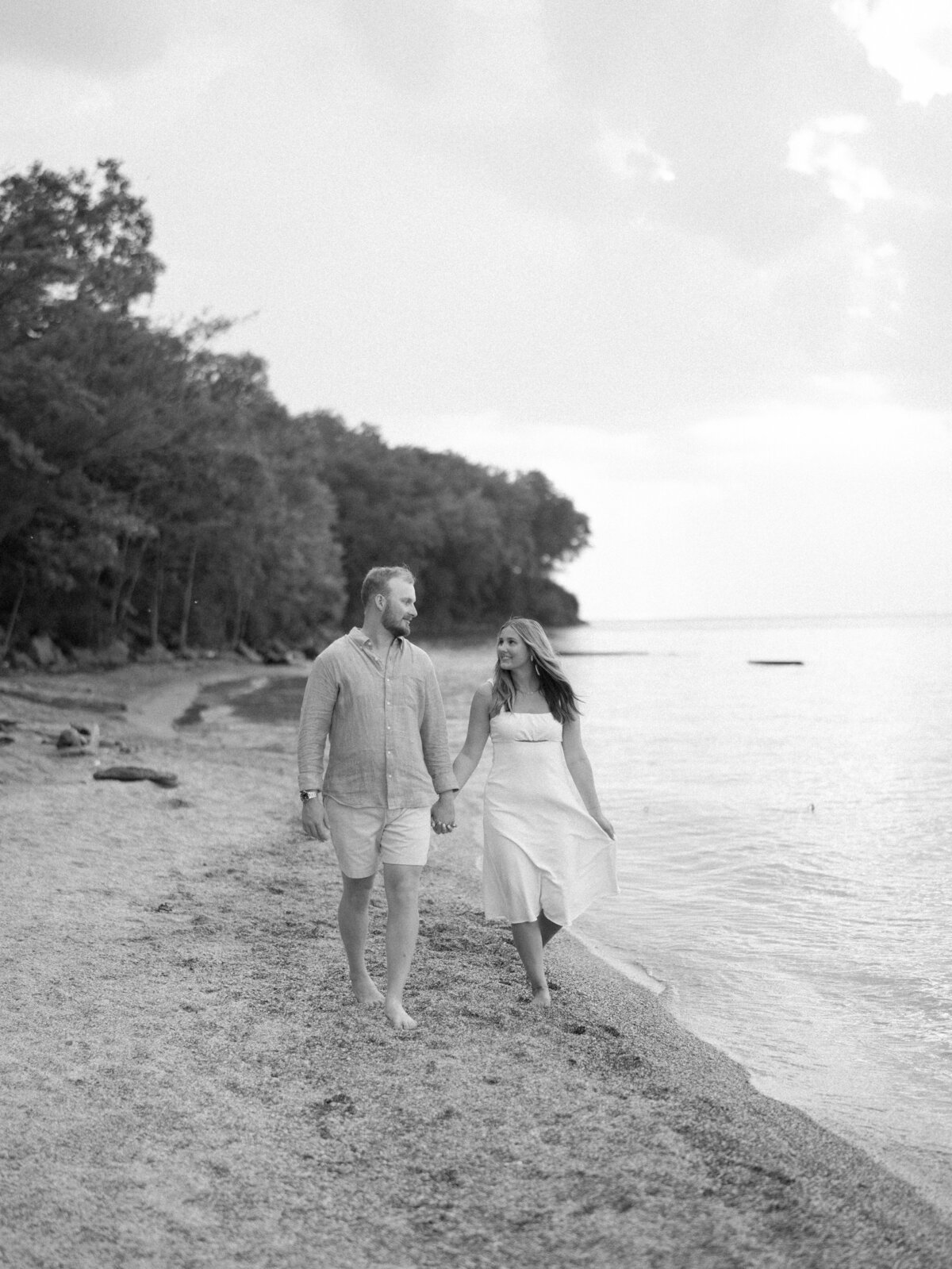 Black and white photo of engaged couple walking along Edgewater Beach shoreline

