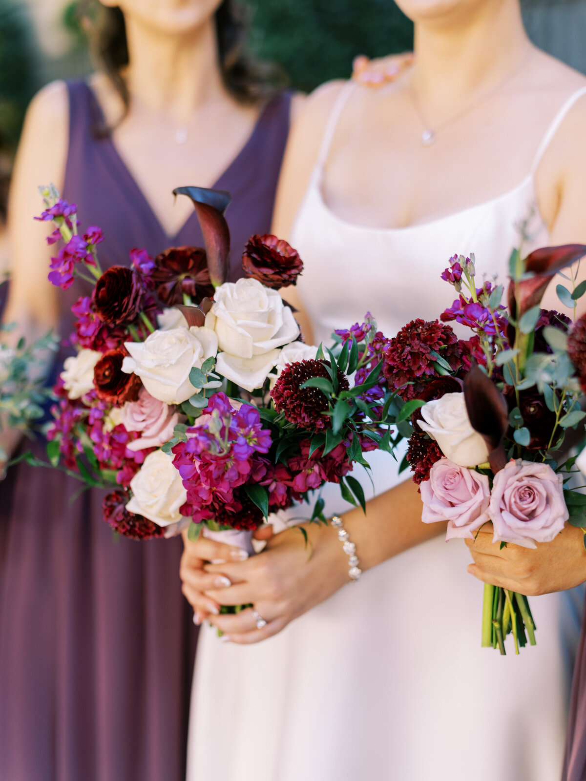 Close-up of bride and bridesmaid holding bouquets of vibrant pink and burgundy jewel toned blooms.