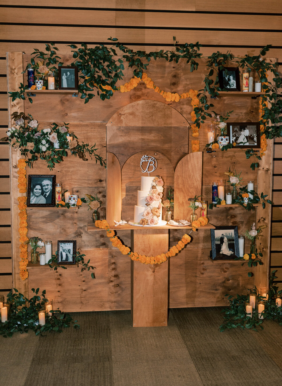 Wooden wedding reception backdrop cake display decorated with photo frames, florals and greenery