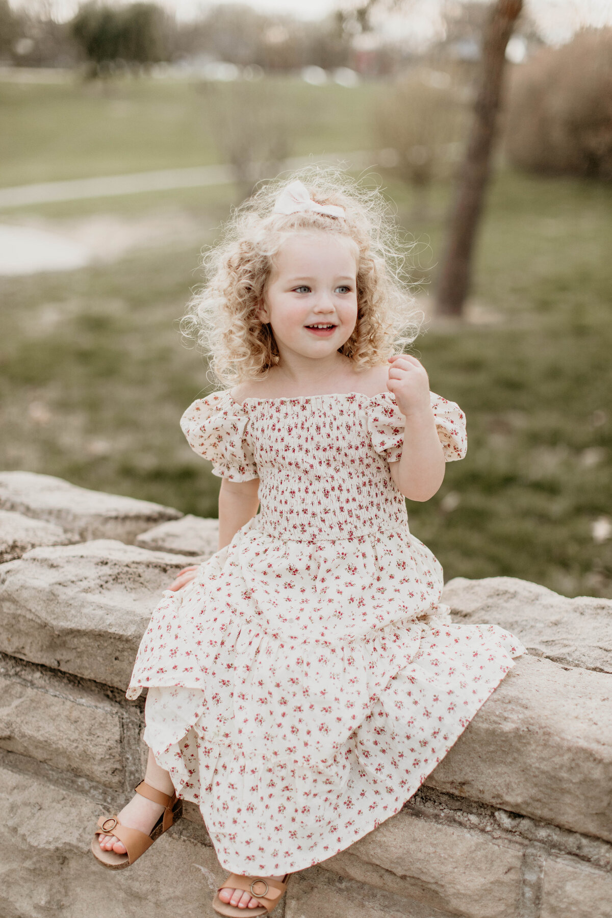 Toddler girl sits on stone railing and laughing. 