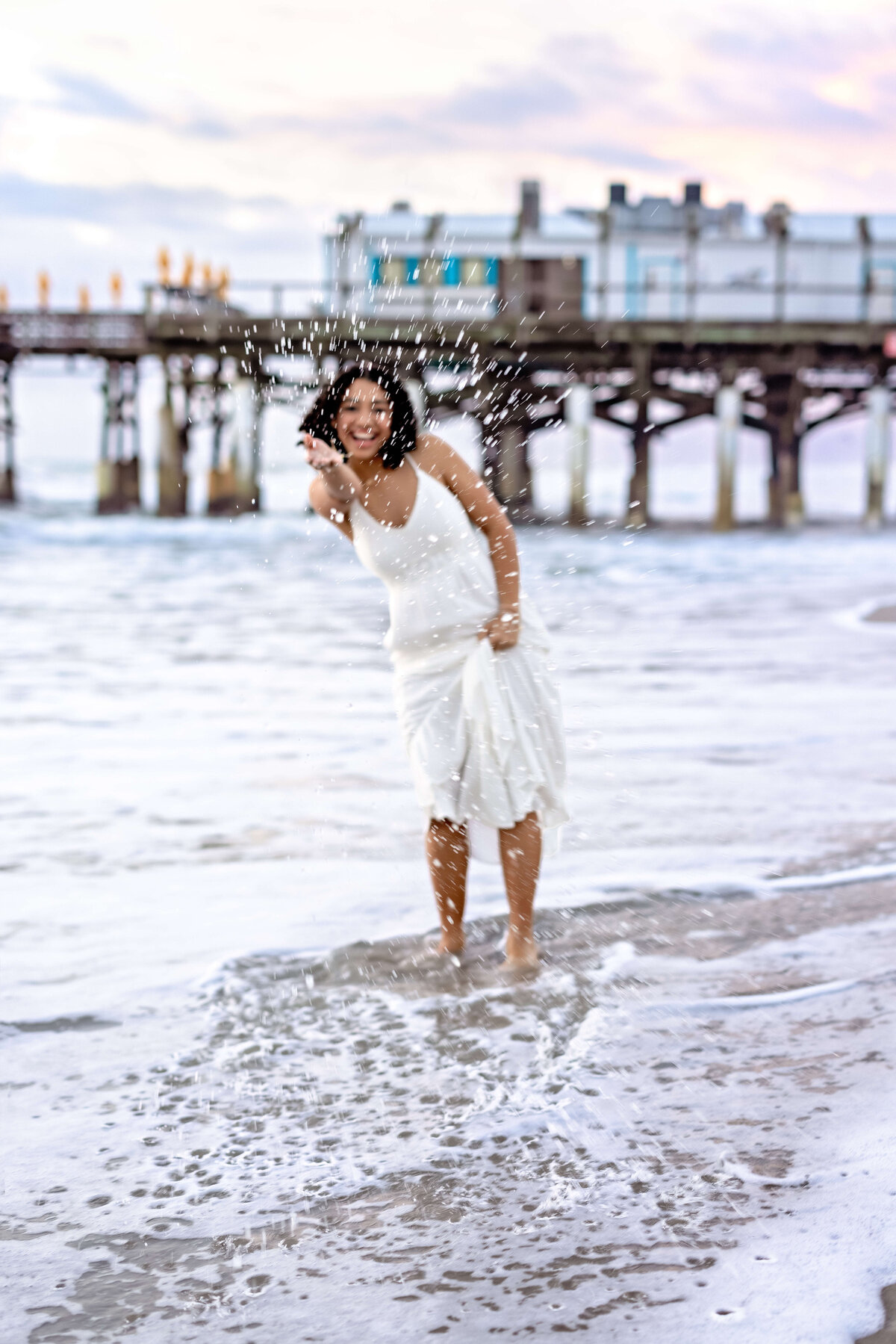 Cocoa Beach senior session with a teen girl splashing water with her hands, laughing and playful in the morning light.