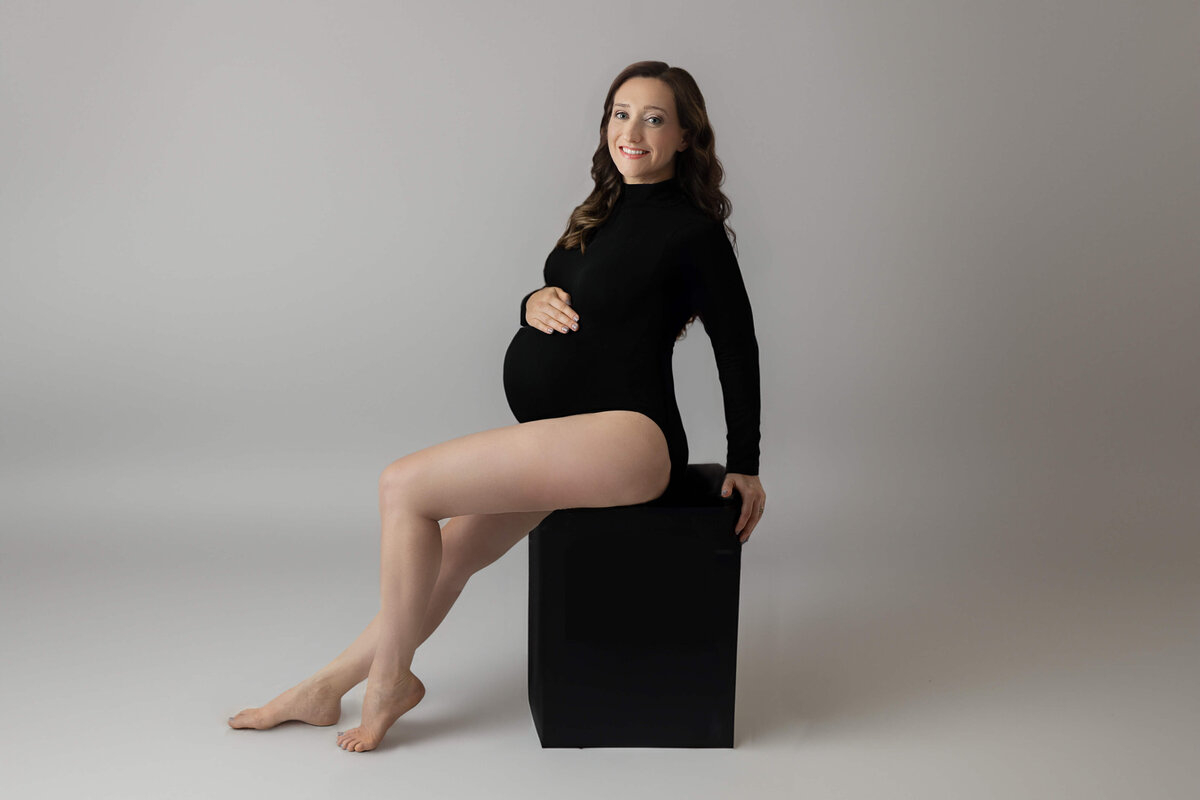 expecting mother in a leotard sitting on a black stool during her maternity session