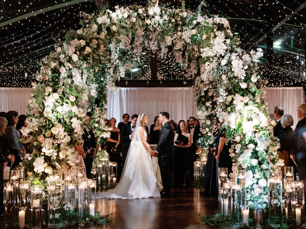 The bride and groom at the ceremony under a floral awning. 