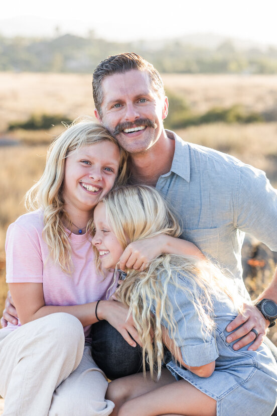 daughters-and-father-laughing-family-of-four-sitting-on-rock-wrights-field-san-diego