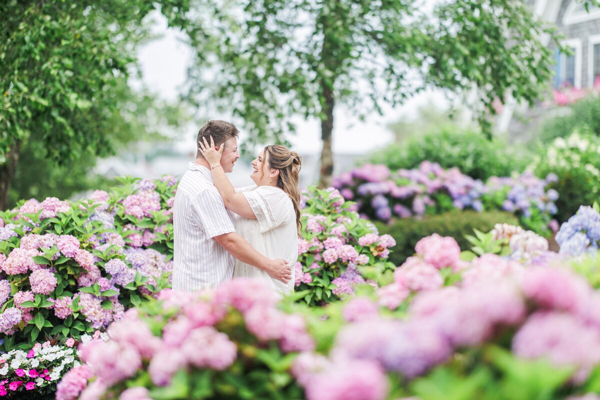 Couple embracing in a garden filled with pink, purple, and blue hydrangeas, smiling closely together, taken at Chatham Bars Inn in Chatham, Massachusetts — representing the portfolio of a Cape Cod engagement photographer.