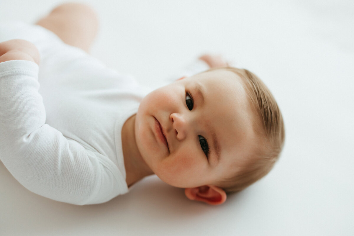 baby boy in white outfit lays in studio