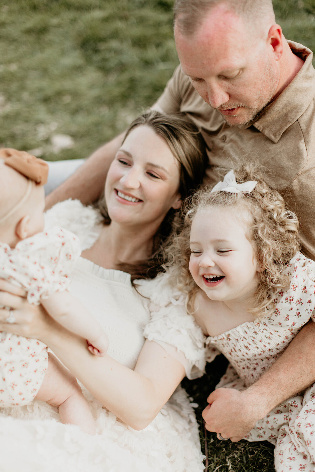 Close up of mom lying in dad's lap while two daughters laugh and look at each other. 