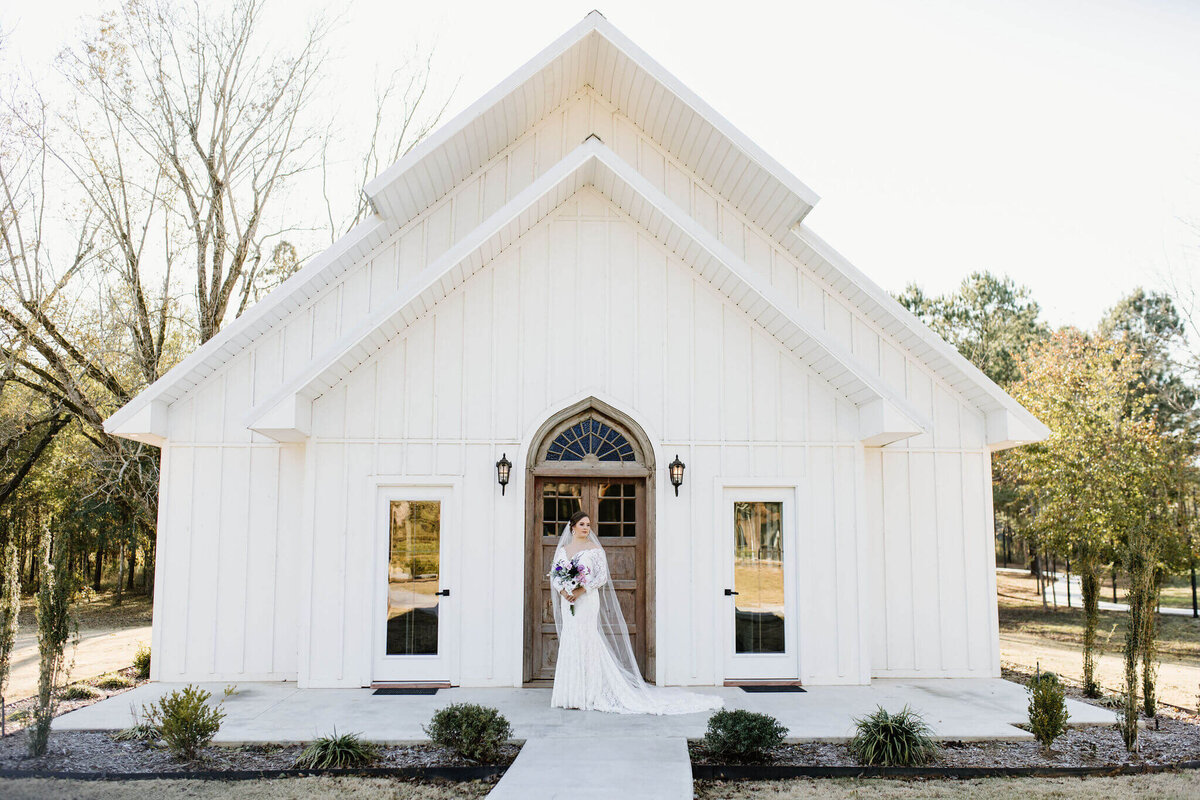 Bridal portrait of bride on wedding day wearing long white wedding dress standing in front of wedding chapel at Four Fifteen Estates Wedding Venue in New Boston, TX