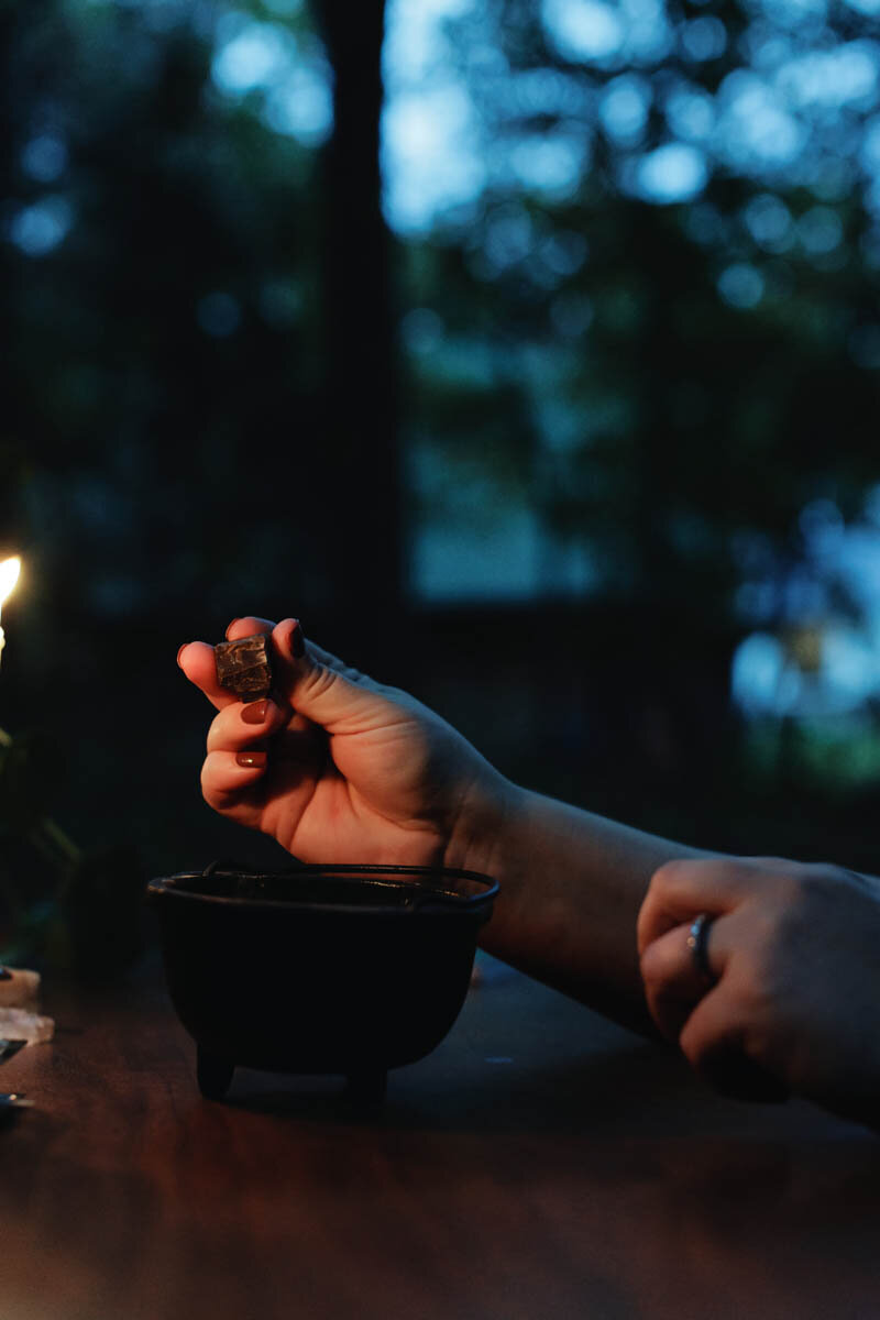 Energy worker Ash Stinson sits by candlelight and drops a small stone into an iron cauldron
