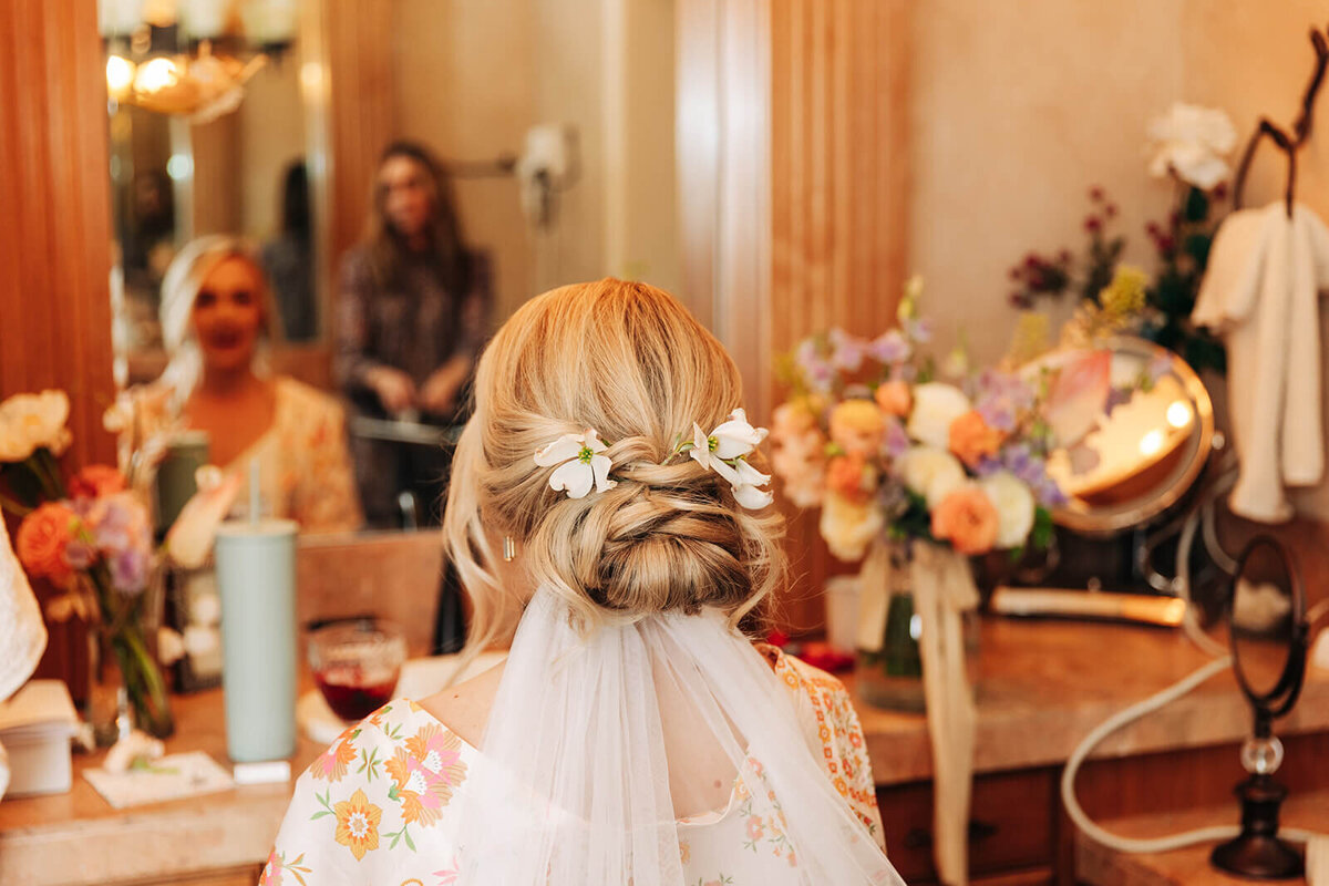 The back of a bride's hair and her blurred reflection as she looks into a mirror.