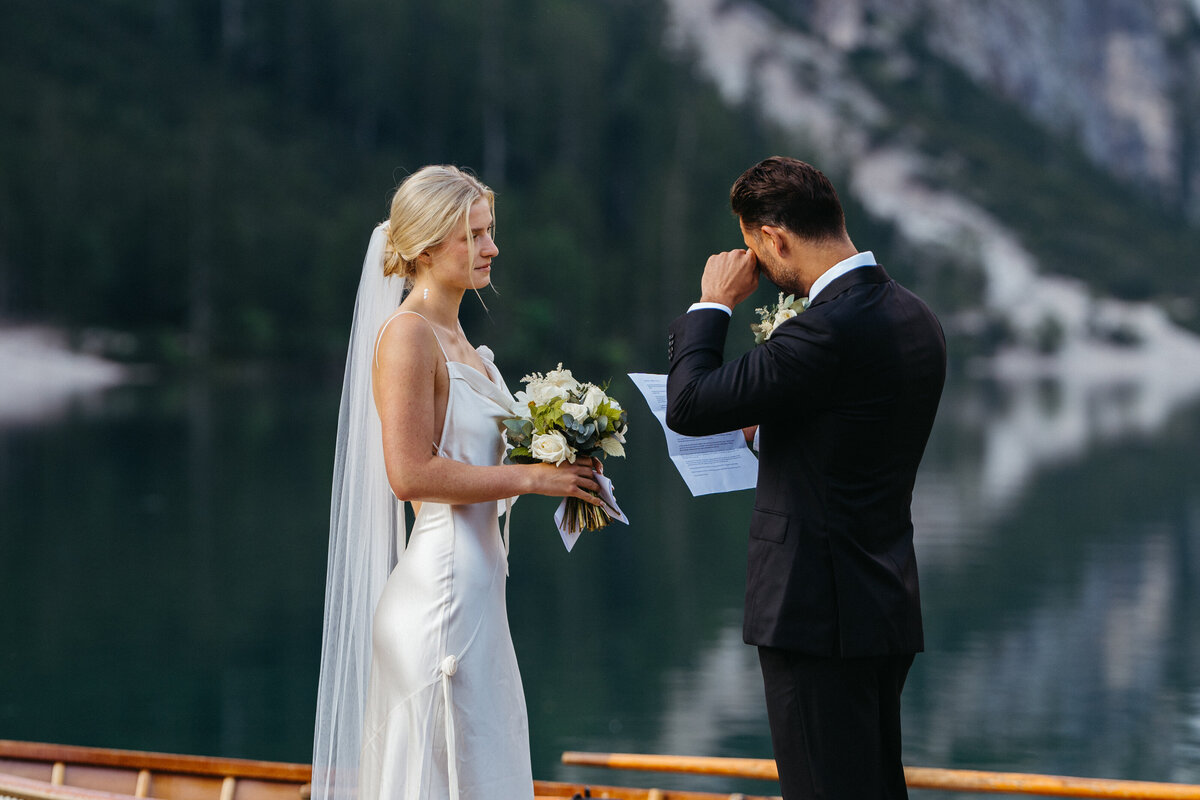 Groom wiping tears as bride holds bouquet during vows
