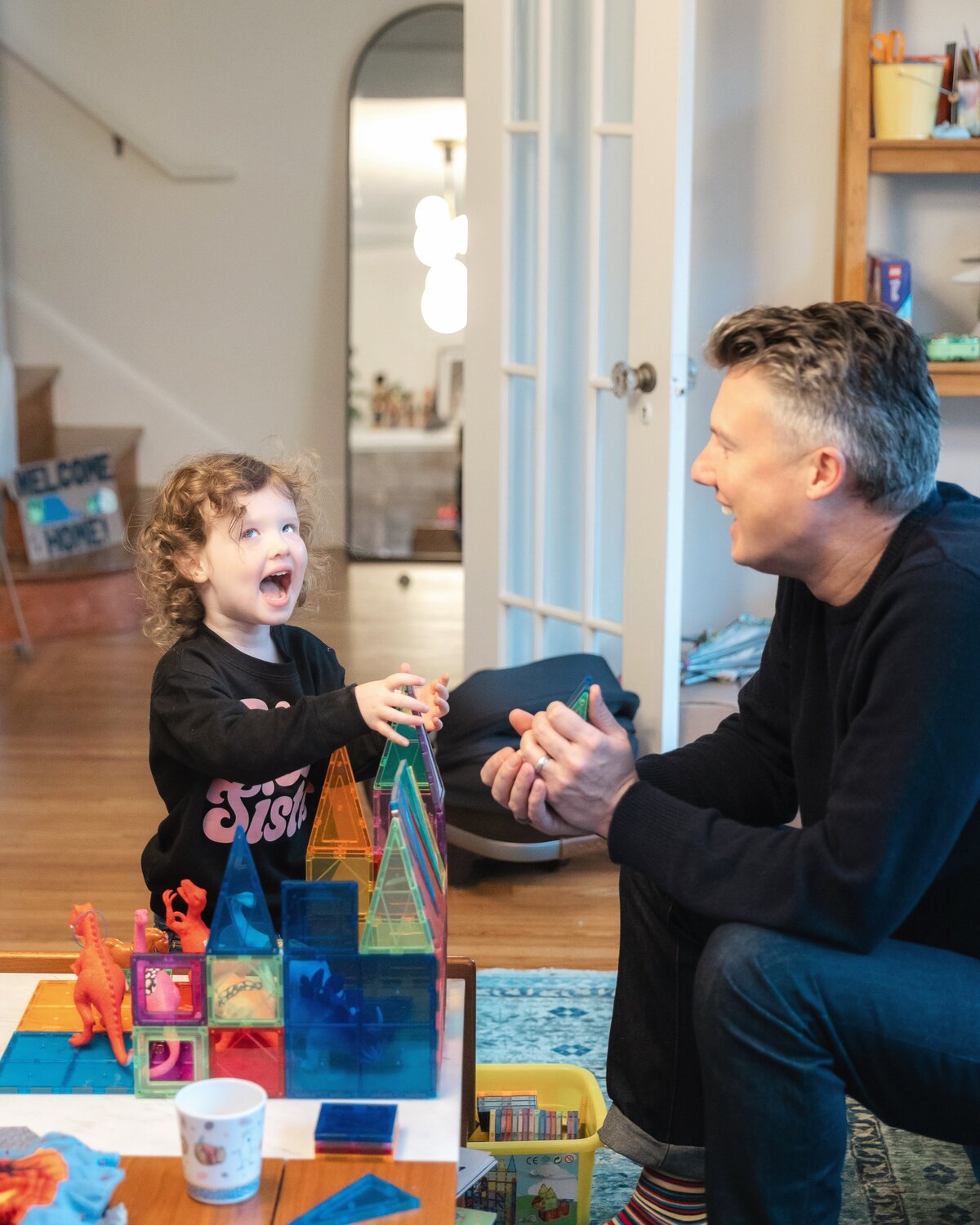 Daughter laughs while building magnatiles with her father