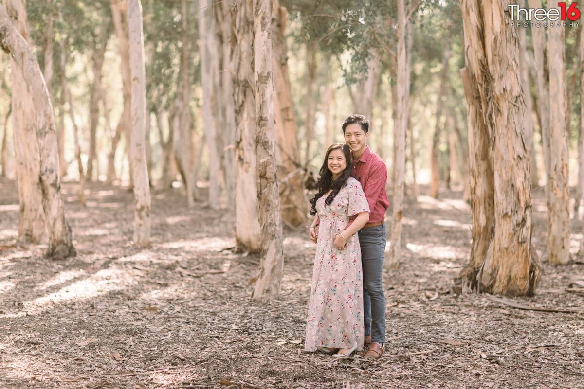 Engaged couple pose for engagement photos amongst the tall trees at Serrano Creek Park