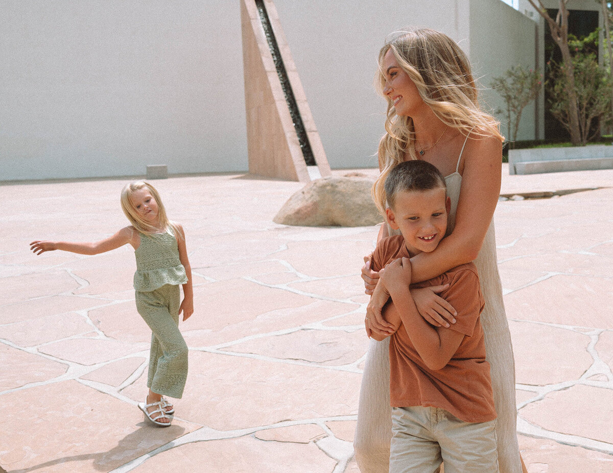 Candid Irvine family photo of a mother hugging her son while her daughter smiles during a session at Noguchi Garden in Orange County.