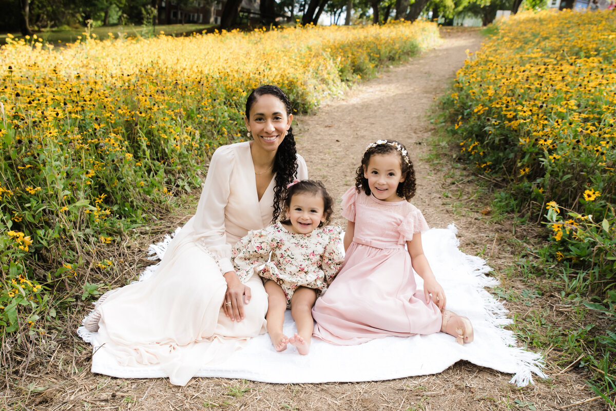 mom sits with two daughters on blanket in wildflower field