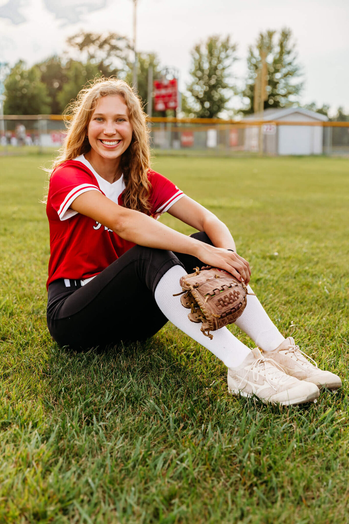 high school softball player sitting in the outfield with her glove