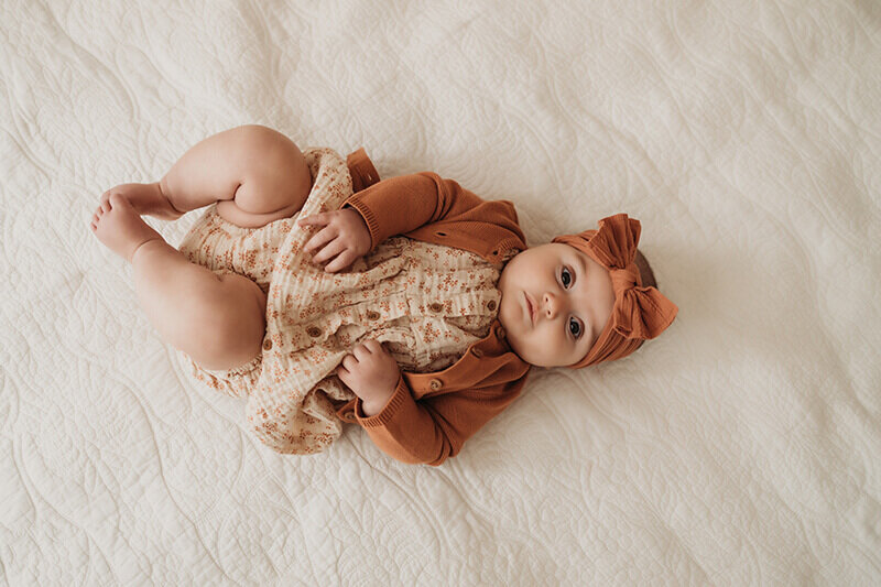 four month old baby girl lays on her back for milestone photo session