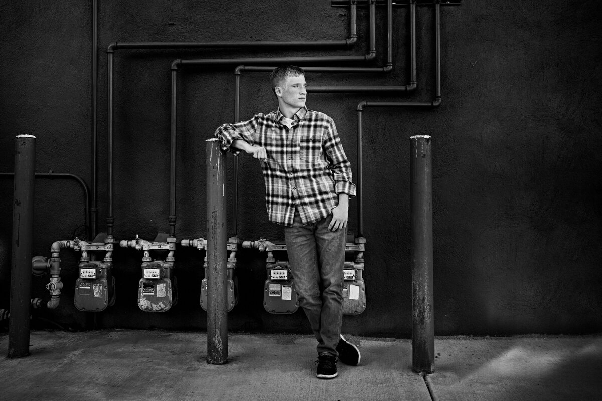 high school senior boy in black and white wearing plaid shirt leaning against metal pole