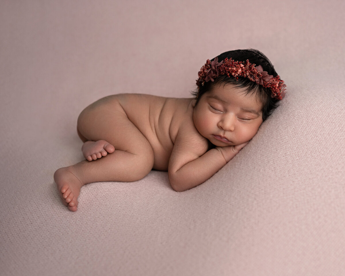 Newborn baby girl posed on pink backdrop with rust floral headband | Austin newborn photographer serving Buda and Westlake