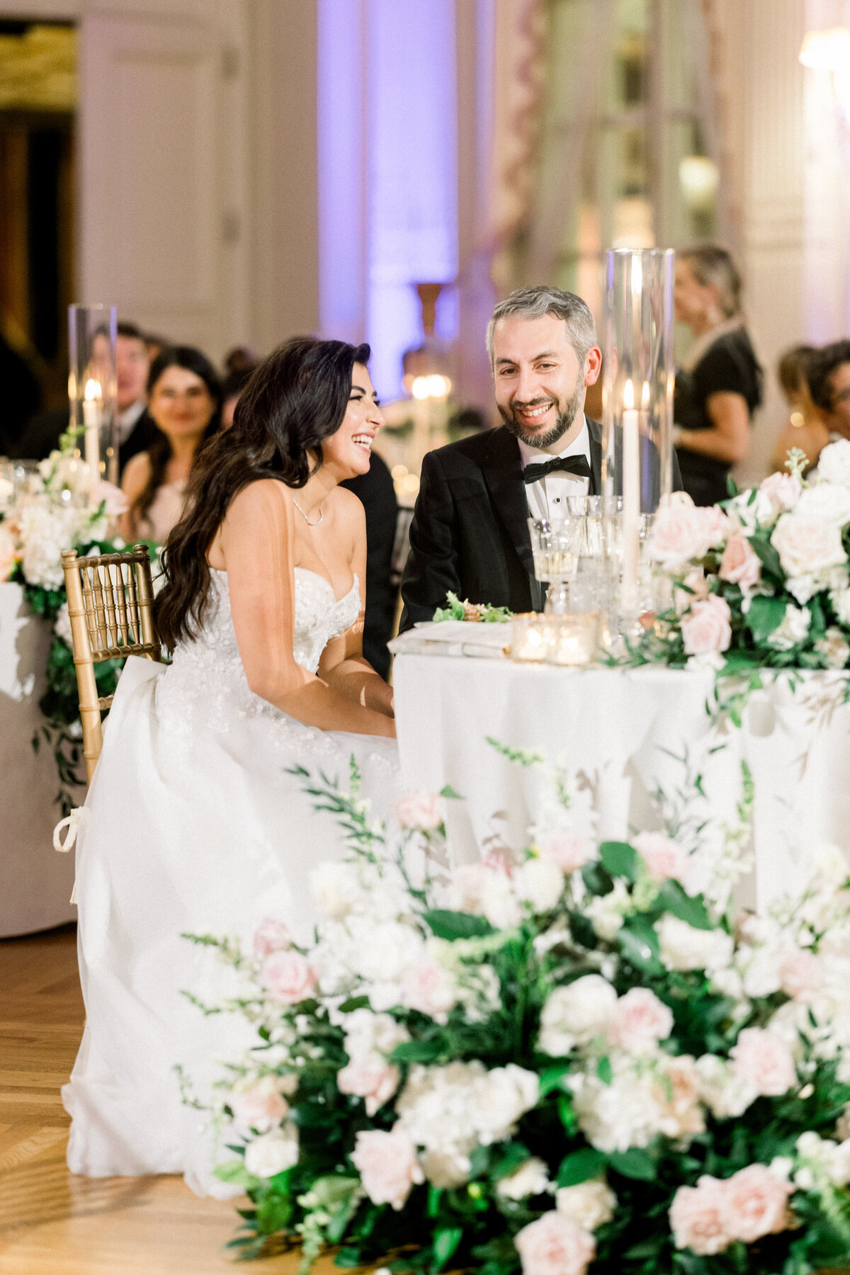 bride and groom sit at sweetheart table and laugh together during maid of honor speech at rosecliff mansion 