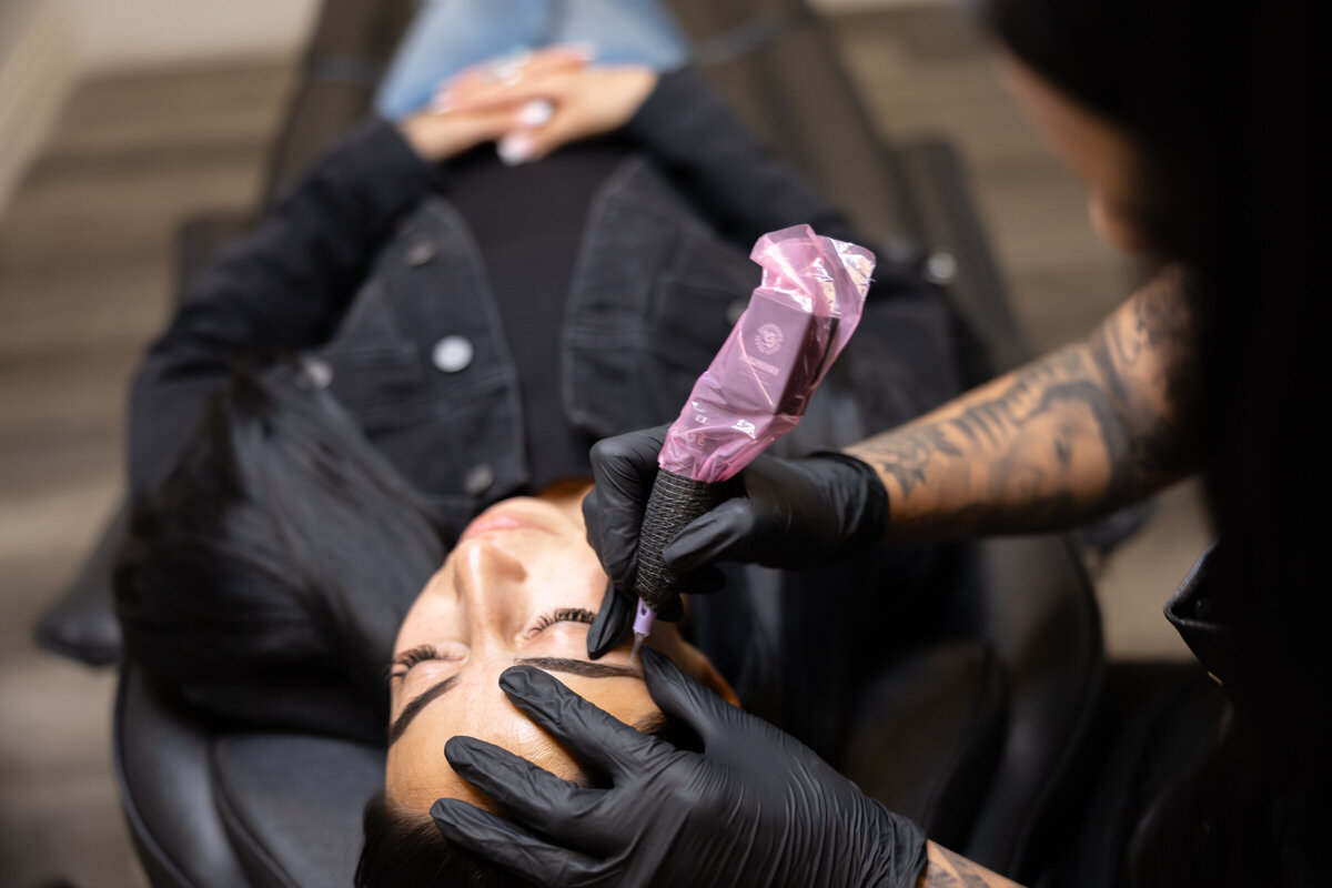 Tattooed brow artist holding tool while focusing on client’s brows. Photograph by Yucaipa branding photographer Kaitlyn Dawn Photography.