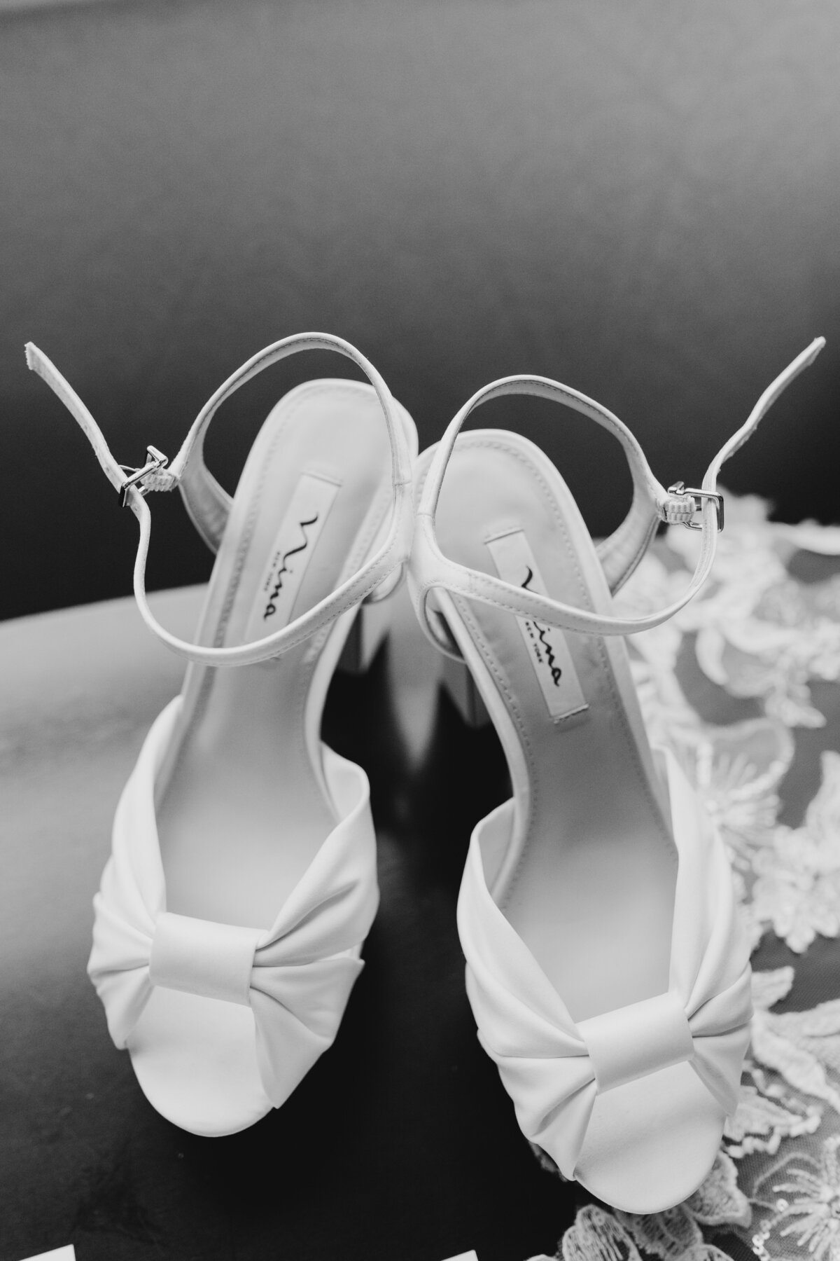 Elegant bridal shoes placed together with lace details in a timeless black and white photo.