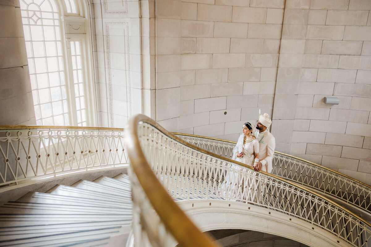 Indian bride and groom on a grand staircase gazing out a floor to ceiling window