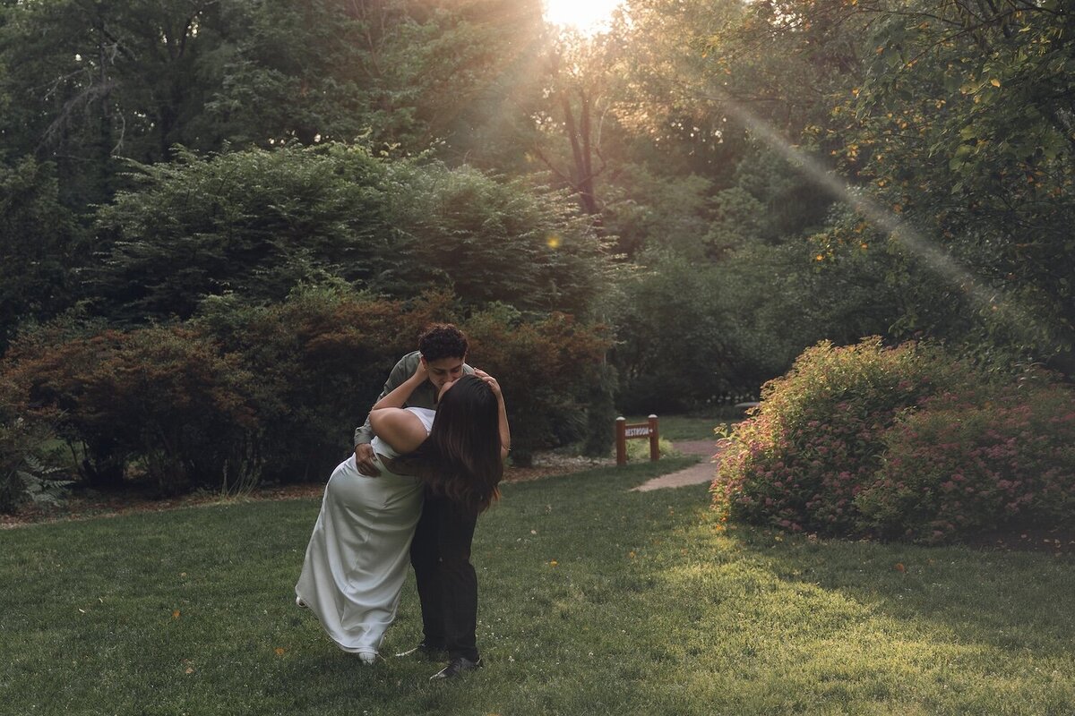 Bride-to-be smiling at groom-to-be under sunset light through the trees.