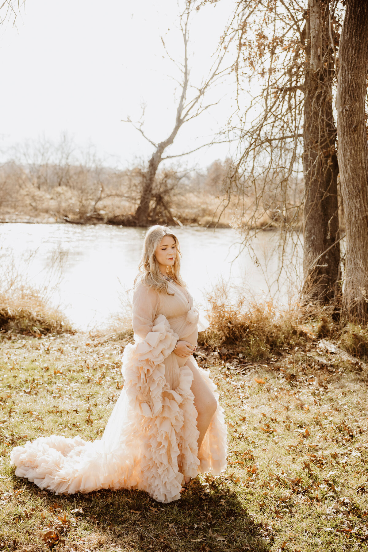 A pregnant woman wears an elegant dress amidst the warm fall woods.