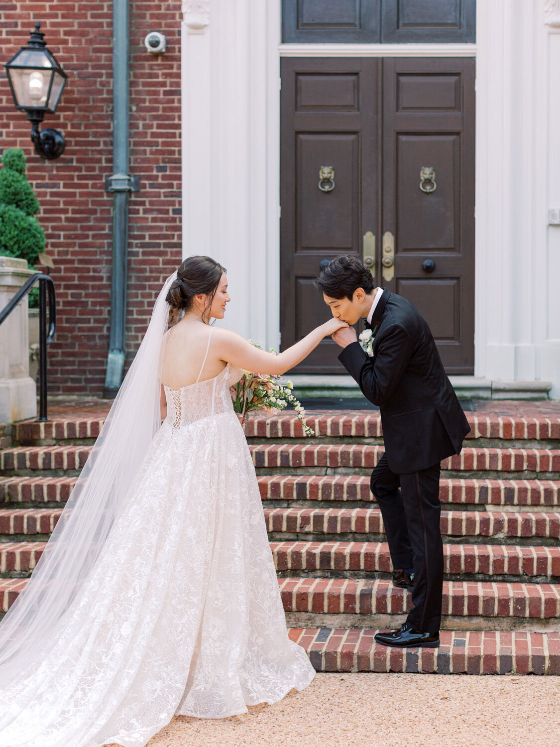 Groom kissing bride’s hand on church steps