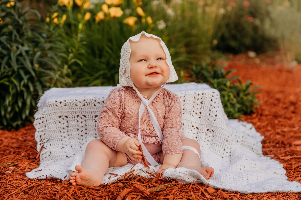 baby girl in bonnet outside by flowers