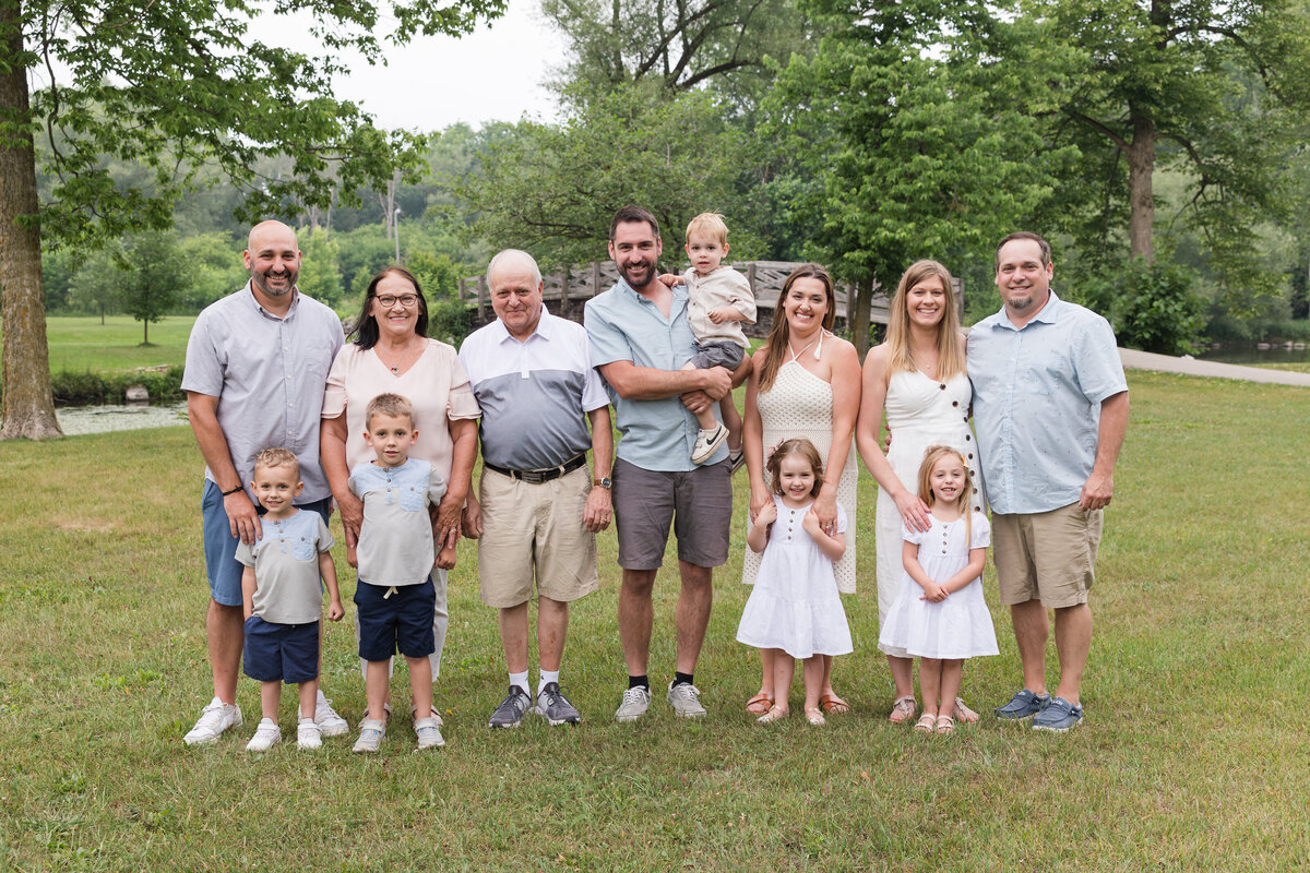 An extended family is standing in a line at a park and smiling at the camera