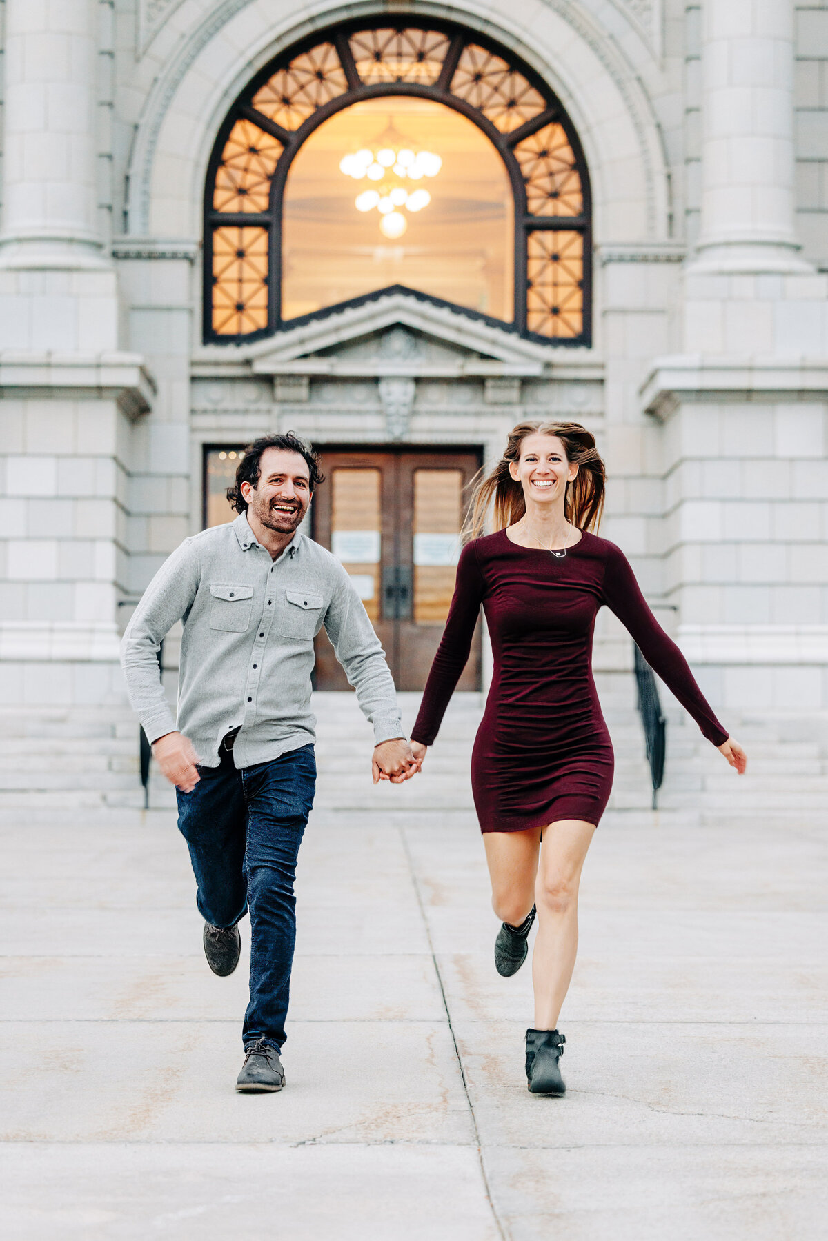 Engaged couple running in front of Missoula County Courthouse